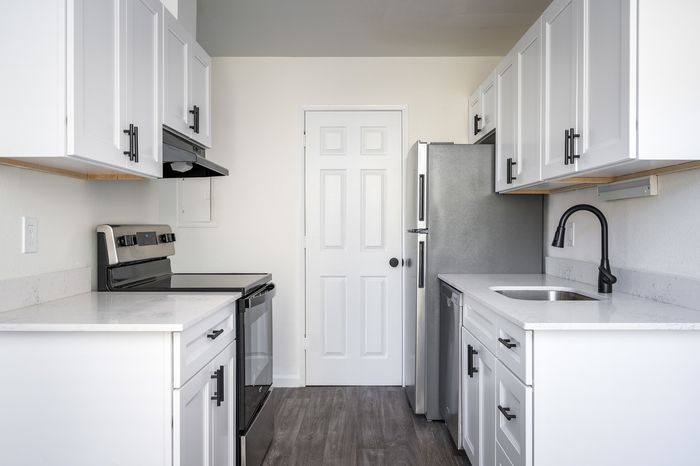 Newly renovated kitchen with white sharker cabinets, wood-inspired flooring, white hard-surface countertops, black fixtures and stainless steel appliances