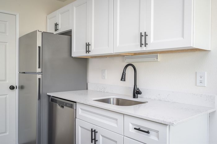 Newly renovated kitchen with white sharker cabinets, wood-inspired flooring, white hard-surface countertops, black fixtures, stainless steel appliances, and a farmhouse-style sink