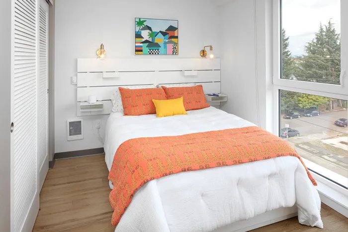 bedroom with vinyl wood like flooring and bed with orange accent pillows at aniva apartments