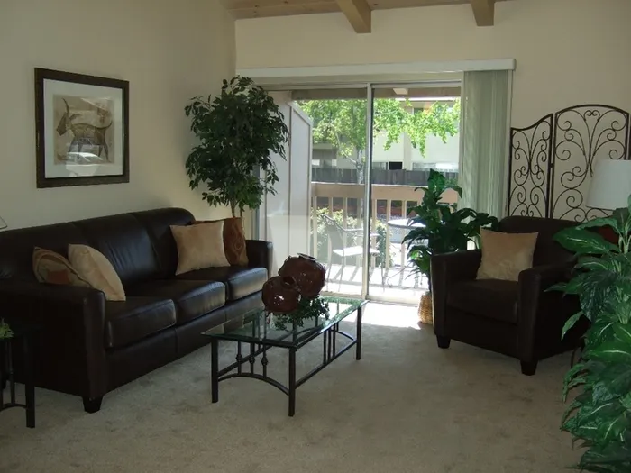 carpeted living room with leather sofas and a metal and glass coffee table at plumas garden apartments