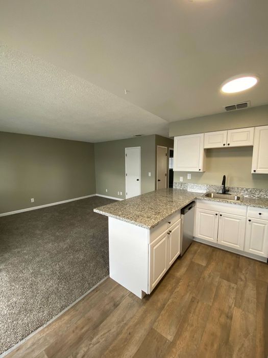 kitchen with black appliances bar area and wood inspired flooring and living room at the creek at south carson