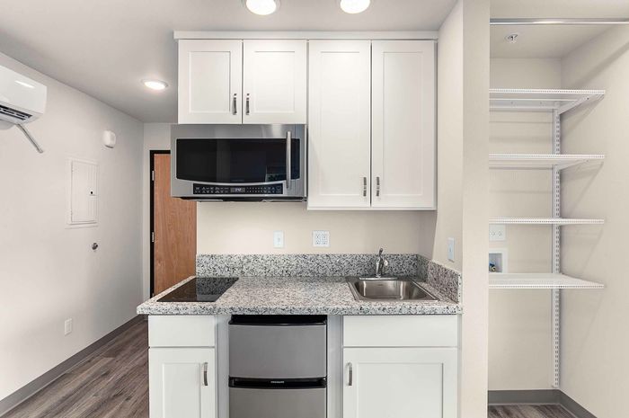 Studio Pointe Kitchen with white cabinets, stone countertops, stainless steel refrigerator and microwave, and 2 burner cooktop.
