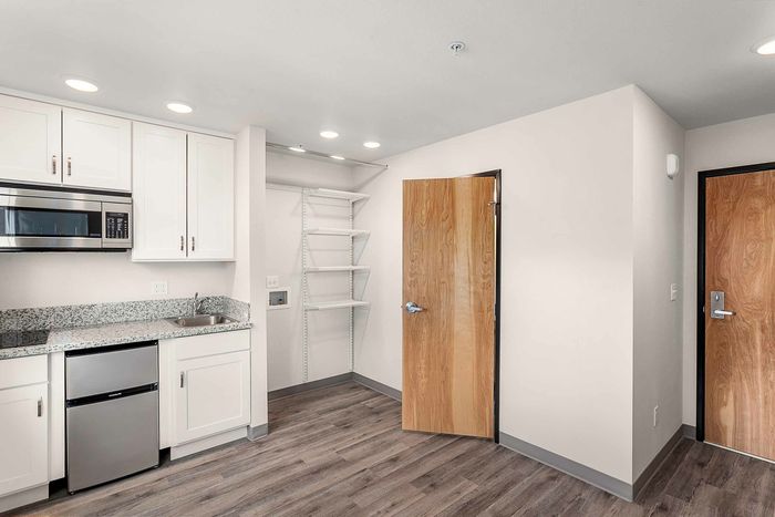 Studio Pointe Kitchen with white cabinets, stone countertops, stainless steel refrigerator and microwave, and 2 burner cooktop. Also includes built-in shelving