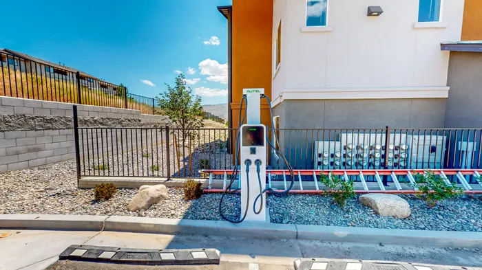 Dog-Friendly Apartments in Reno, NV - Canyon's Edge Apartments - EV Charging Station Beside An Apartment Building With Utility Meters, Metal Fencing, Rock Landscaping, And Blue Sky.