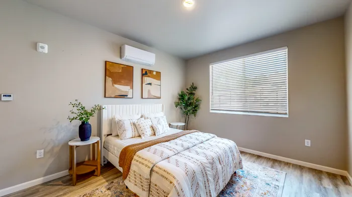 Reno, NV, Apartments with In-Unit Washer and Dryer - Canyon's Edge Apartments - Bedroom With White Bedframe, Patterned Bedding, Side Tables With Plants, Large Window, And Wood Style Flooring.