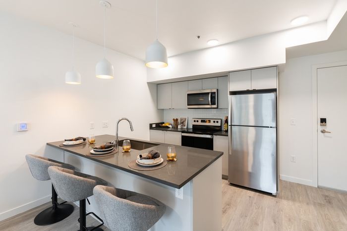 Milwaukie, OR Pet-Friendly Apartments - Henley Place - Kitchen With Quartz Countertops, Whirlpool Stainless Steel Appliances, Luxury Vinyl Flooring, Kitchen Tile Backsplash, And Breakfast Bar