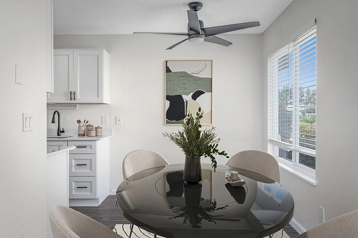 virtually staged kitchen with a ceiling fan and white cabinets and a round dining table with beige chairs