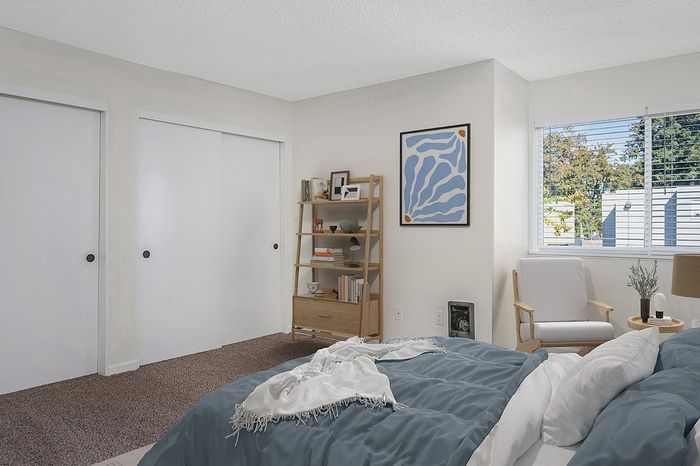 virtually staged bedroom with brown carpet sliding closet doors and bed with blue comforter and an arm chair at its corner
