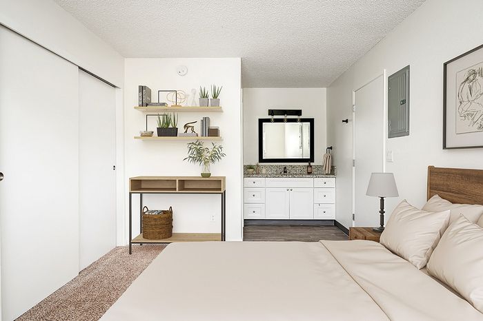 virtually staged bedroom with brown carpet sliding closet doors and bed with beige comforter and a dresser at its corner