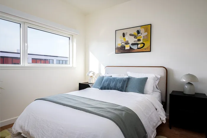 1 Bedroom highrise Apartments in Portland OR - Jute - Furnished Bedroom with White Walls, Wood-Style Flooring, Twin Balck Nightstands, a Large Bed, and a WindowBedroom with ample natural light