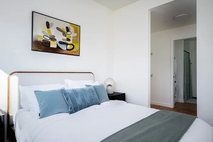 1 Bedroom Apartments In Central Portland OR - Jute - Bedroom With A Queen Bed, Stylish Wall Art, And An En-suite Bathroom Featuring In-unit Washer And Dryer.