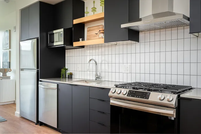 Central Portland OR Studios For Rent - Jute - Kitchen With Stainless Steel Appliances, Gas Range, Microwave, Dishwasher, Dark Cabinetry, White Tile Backsplash, and Sleek Countertops