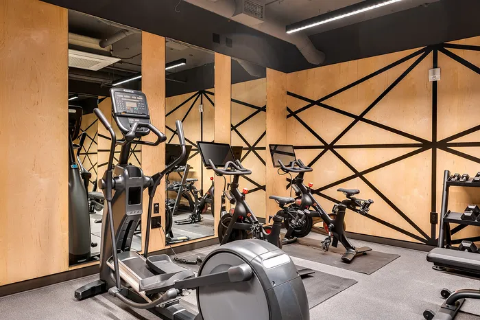 Pet-Friendly Luxury Apartments In Portland Or - Jute - Fitness Center With Cardio Equipment, Mirrored Walls, Wood Paneling, and Contemporary Lighting.