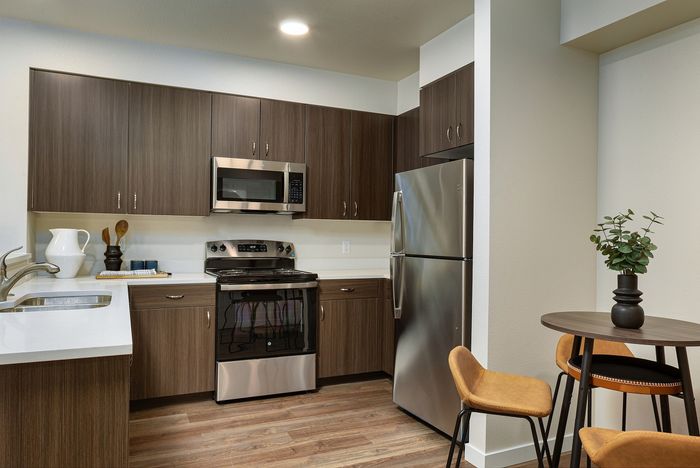 Apartments in Albany, OR with In-Unit Washer and Dryer - Creekside Meadows - Kitchen with Cabinetry, Countertops, Backsplash, Fully Equipped with Stainless Steel Appliances, a Table, and Chairs.