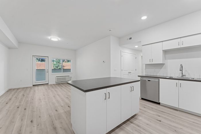 Kitchen and living area with wood-style flooring, stainless steel appliances and kitchen island.