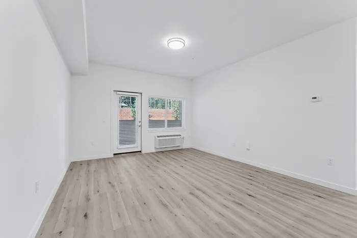 Living area with wood-style flooring, a door leading to a patio, and an air conditioner