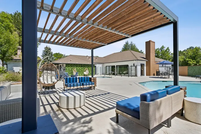 1-Bedroom Apartments in South Reno, NV - Redfield Ridge - Poolside Outdoor Lounge With Sofa Seating, Hanging Chair, Coffee Table, and Wooden Pergola Beside The Community Pool.