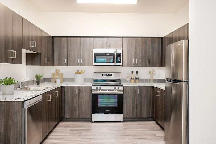 Tigard, OR, Apartments Near Washington Square Mall - Pacific Ridge Apartments - Kitchen with Custom Cabinetry, Energy-Efficient Stainless Steel Appliances, Wood-Style Flooring, and Light Fixture.