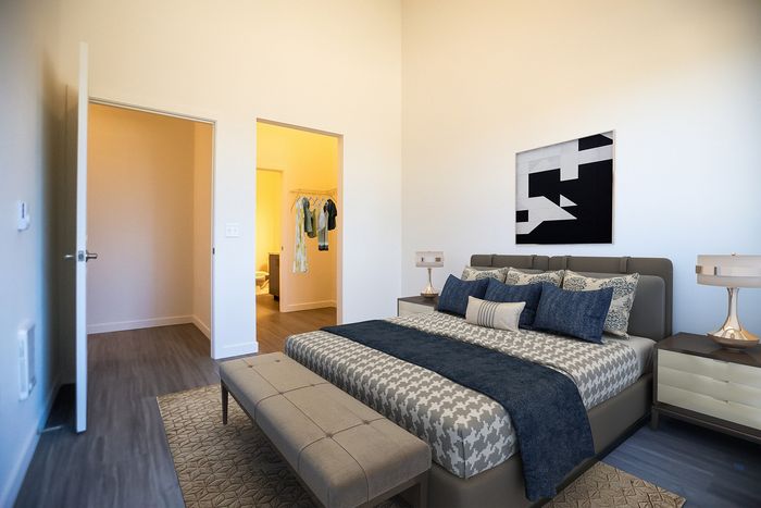 Apartments in Tigard, OR, with In-Unit Washer and Dryer - Pacific Ridge Apartments - Bedroom with Wood-Style Flooring, Large Bed, Bed Bench, Wall Art, Nightstands, Lamps, and Oversized Closet.