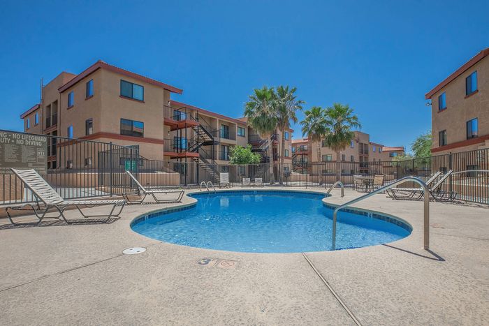 pool with lounge chairs and three story apartment buildings in the back