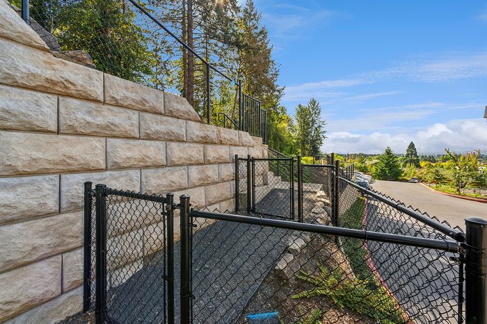 Dog-Friendly Apartments in Tigard, OR - Pacific Ridge Apartments - A Dog Run with a Retaining Wall, Sloped Ground, and Enclosed in a Black Metal Fence.