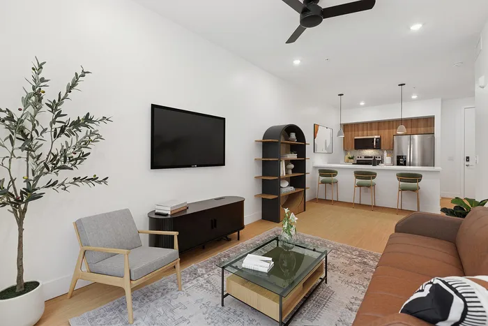Pet-Friendly Luxury Apartments In Midtown Phoenix, AZ - Asa Midtown - Living Room with a Dark Sectional Couch, Armchairs, Glass Coffee Table, Wall-Mounted TV, and a Cowboy Artwork.
