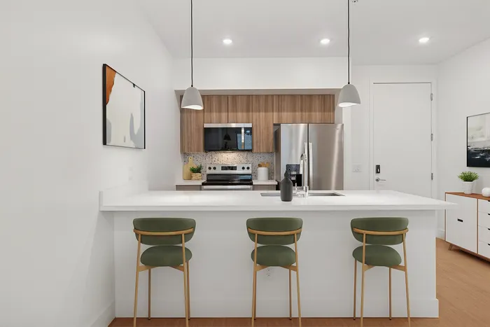 Midtown Phoenix, AZ, Luxury Apartments with In-Unit Washer and Dryer - Asa Midtown - A Sleek Kitchen with Island and Bar Seating, Stainless Steel Appliances, Wood Cabinetry, and Pendant Lighting.