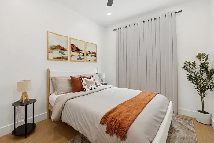 One-Bedroom Luxury Apartments in Midtown Phoenix, AZ - Asa Midtown - A Bedroom with a Queen-Size Bed, Desert-Inspired Artwork, Sleek Nightstands, a Sliding Barn-Style Door, and a Hanging Potted Plant.