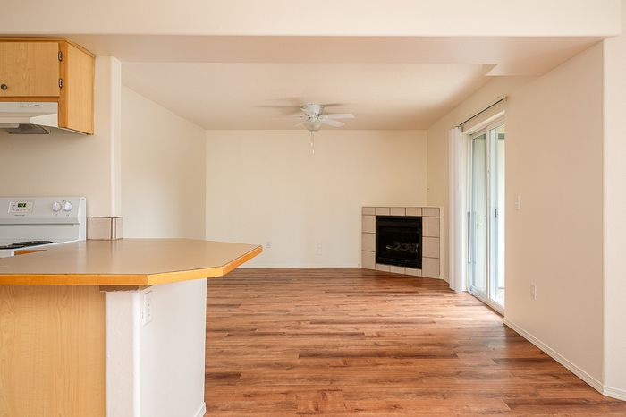 Main living area with fireplace, wooden floor, open plan kitchen, ceiling fan, and patio.