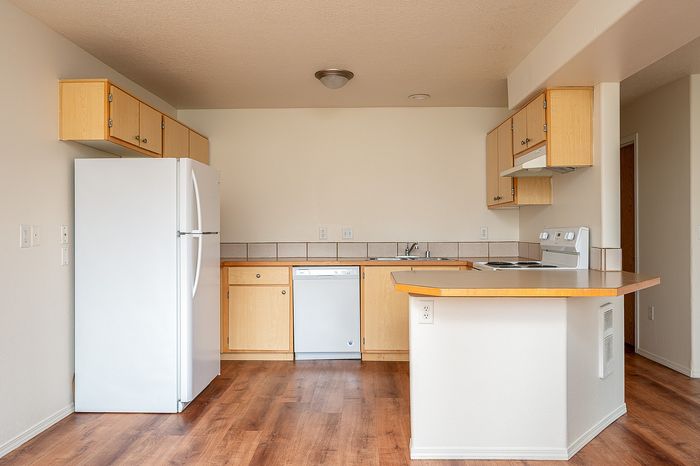 Open plan kitchen area with fridge, disherwasher, oven, stove, countertops, cupboards, and wooden floor.