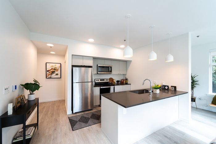 Open plan kitchen area with fridge, microwave, oven, countertops, and white walls.