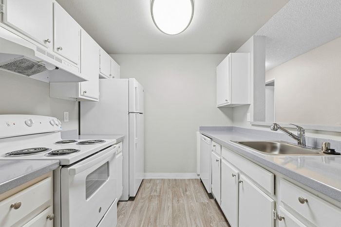galley view of kitchen in C1 renovated floorplan at Timber Flats white cabinets white appliances and grey countertops