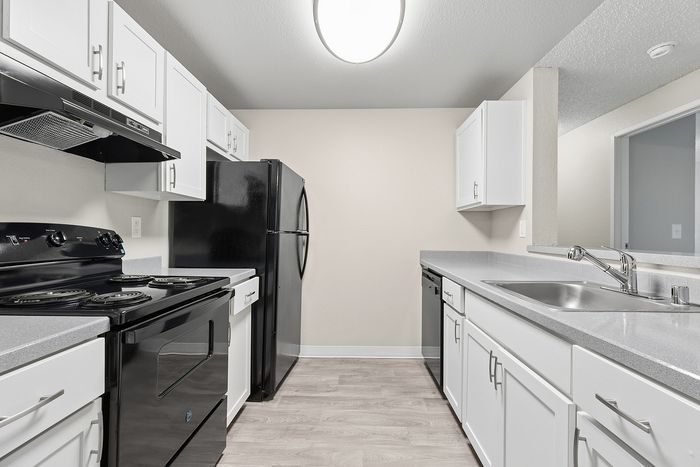 galley view of kitchen in B1 renovated floorplan at Timber Flats white cabinets black appliances and grey countertops