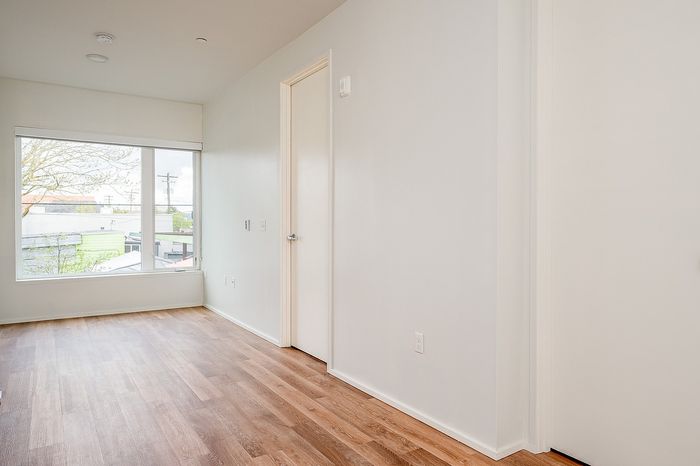One Bedroom at Lyra Apartments - view into the living room with white walls, large window and hardwood floors