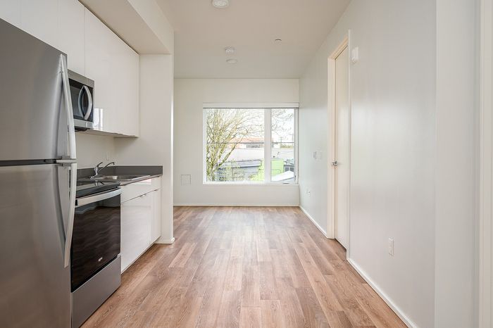 One Bedroom at Lyra Apartments - view from kitchen into the living room with stainless steel appliances and hardwood floors