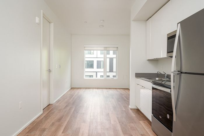 One-Bedroom at Lyra Apartments - view from the kitchen into the living room with stainless steel appliances and hardwood floors