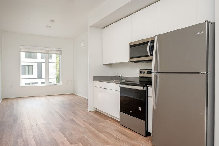 One-Bedroom at Lyra Apartments - view from the kitchen into the living room with stainless steel appliances and hardwood floors