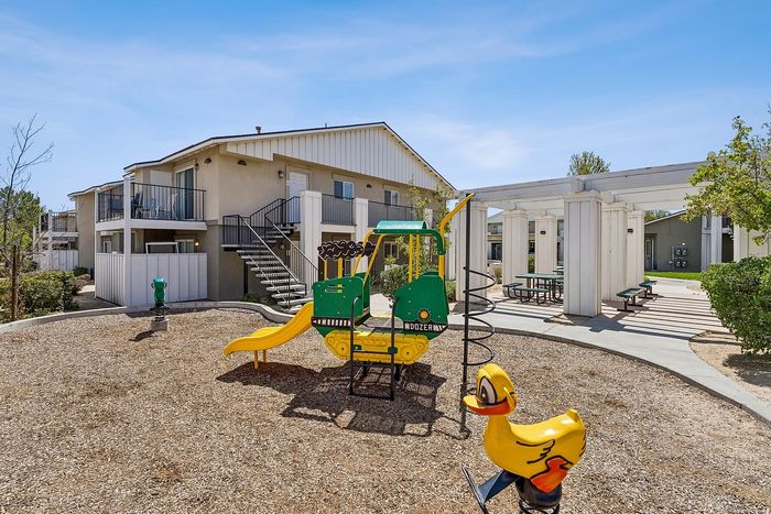 Playground with apartments, community area seating, and blue sky.