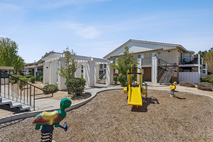 Playground with apartments, trees, sand, and blue sky.