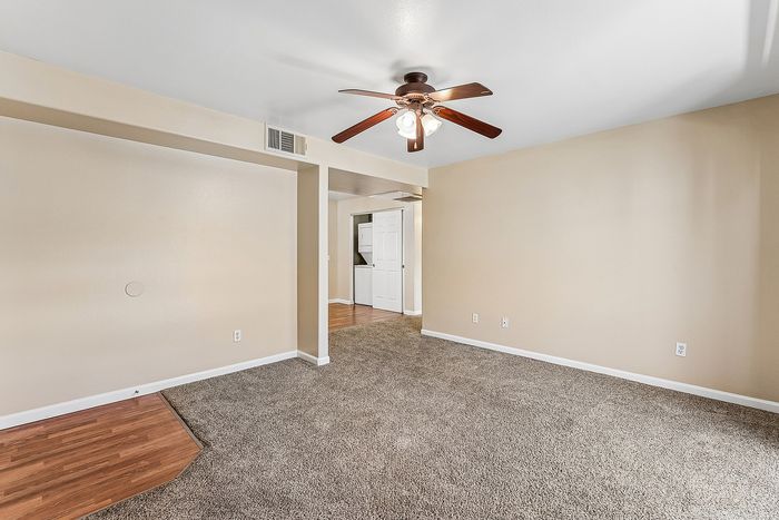 Living space with carpet, wooden floor, ceiling fan, and open space.