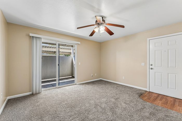 Living space with wooden floor, carpet, ceiling fan, and patio.