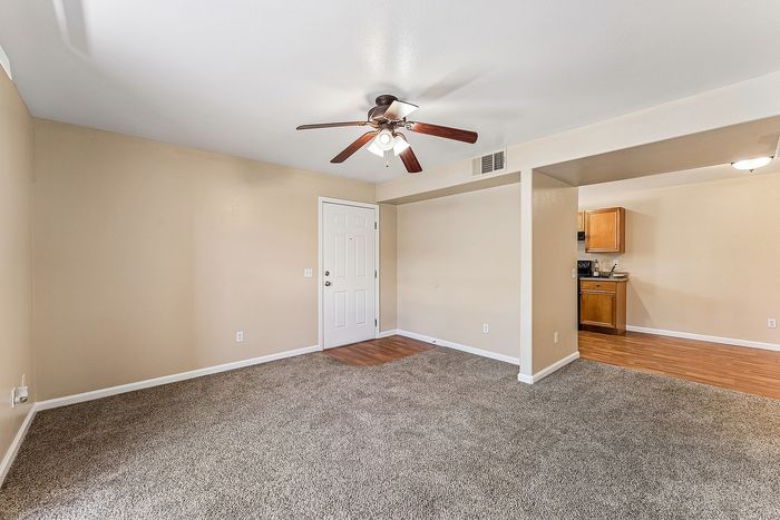 Open plan living area with carpet, wooden floor, ceiling fan, and kitchen.