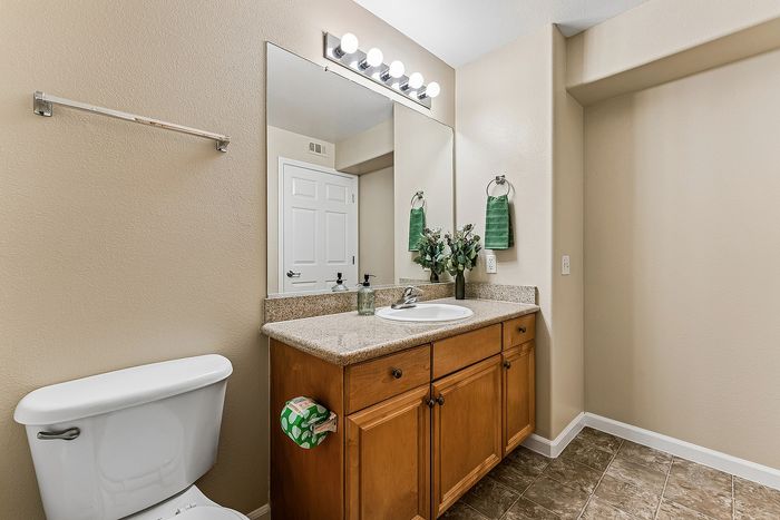 Bathroom with toilet, sink, mirror, wooden counter tops and cupboard.