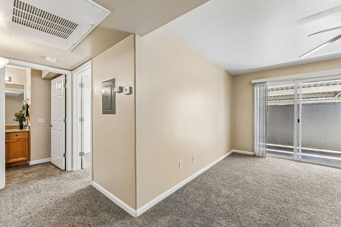 Open living area with carpet, patio, ceiling fan, AC unit, and hallway to bathroom.