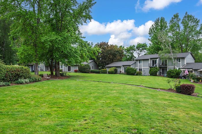 Field with trees, blue sky, and apartments.