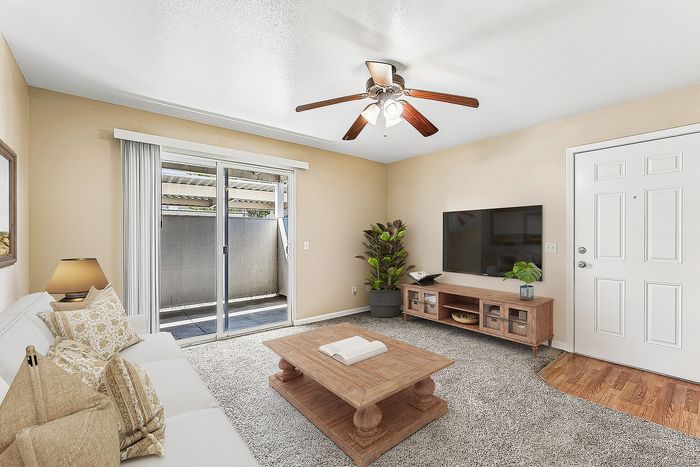 virtually staged living room with sofa, tv, coffee table, ceiling fan, and patio.