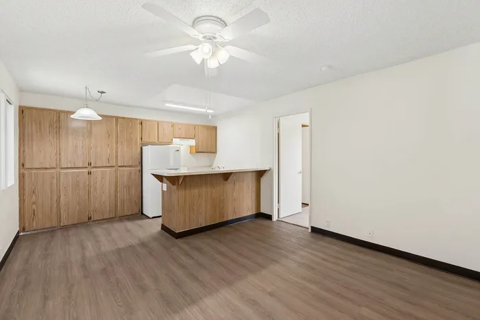 Living room and view into the kitchen at Orchard Mesa with wood floors, wood cabinets, white walls and a ceiling fan