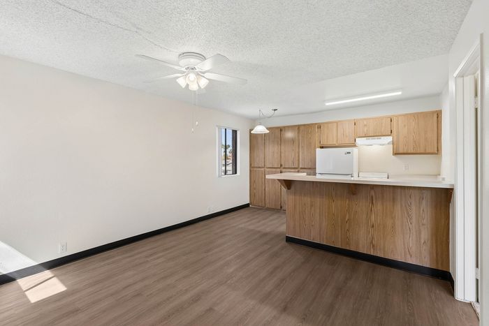 Living room and view into the kitchen at Orchard Mesa with wood floors, wood cabinets, white walls and a ceiling fan
