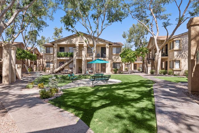 Courtyard at Orchard Mesa with grass, trees and seating with umbrellas