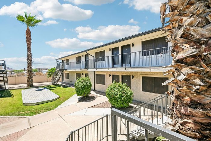 Two-story apartment building at Deer Valley Village with palm trees and metal staircases.